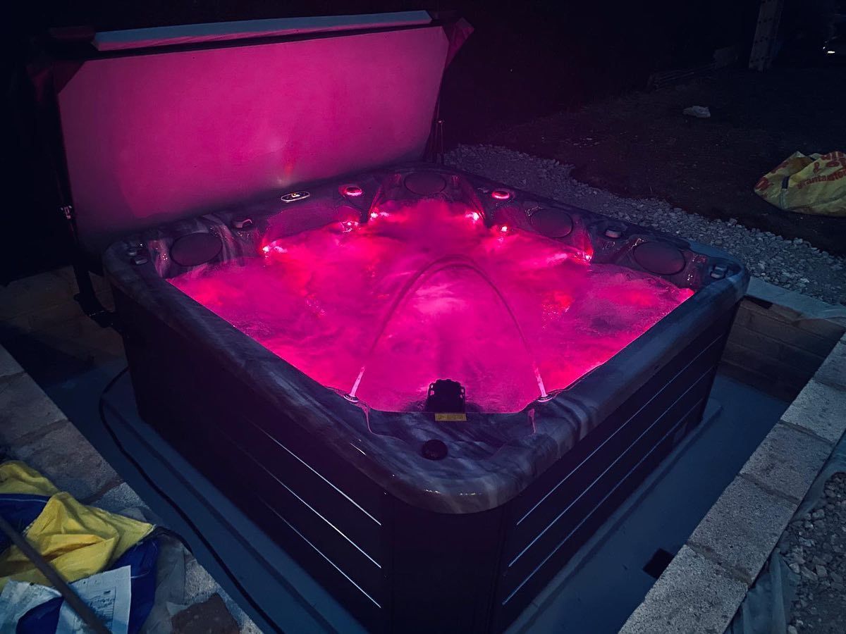 Hot tub at night, lit with pink lights, cover partially open.