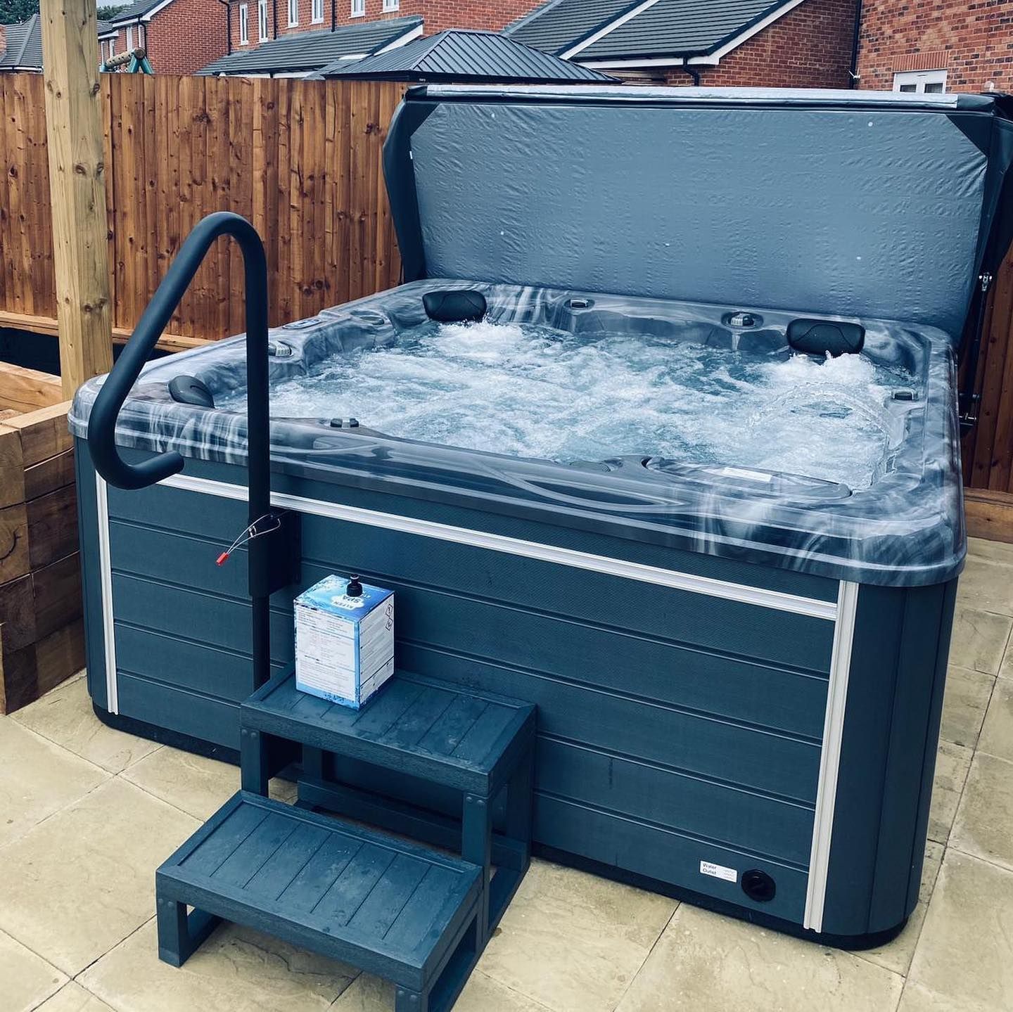 Hot tub filled with water and bubbles, with a lid open, next to steps.
