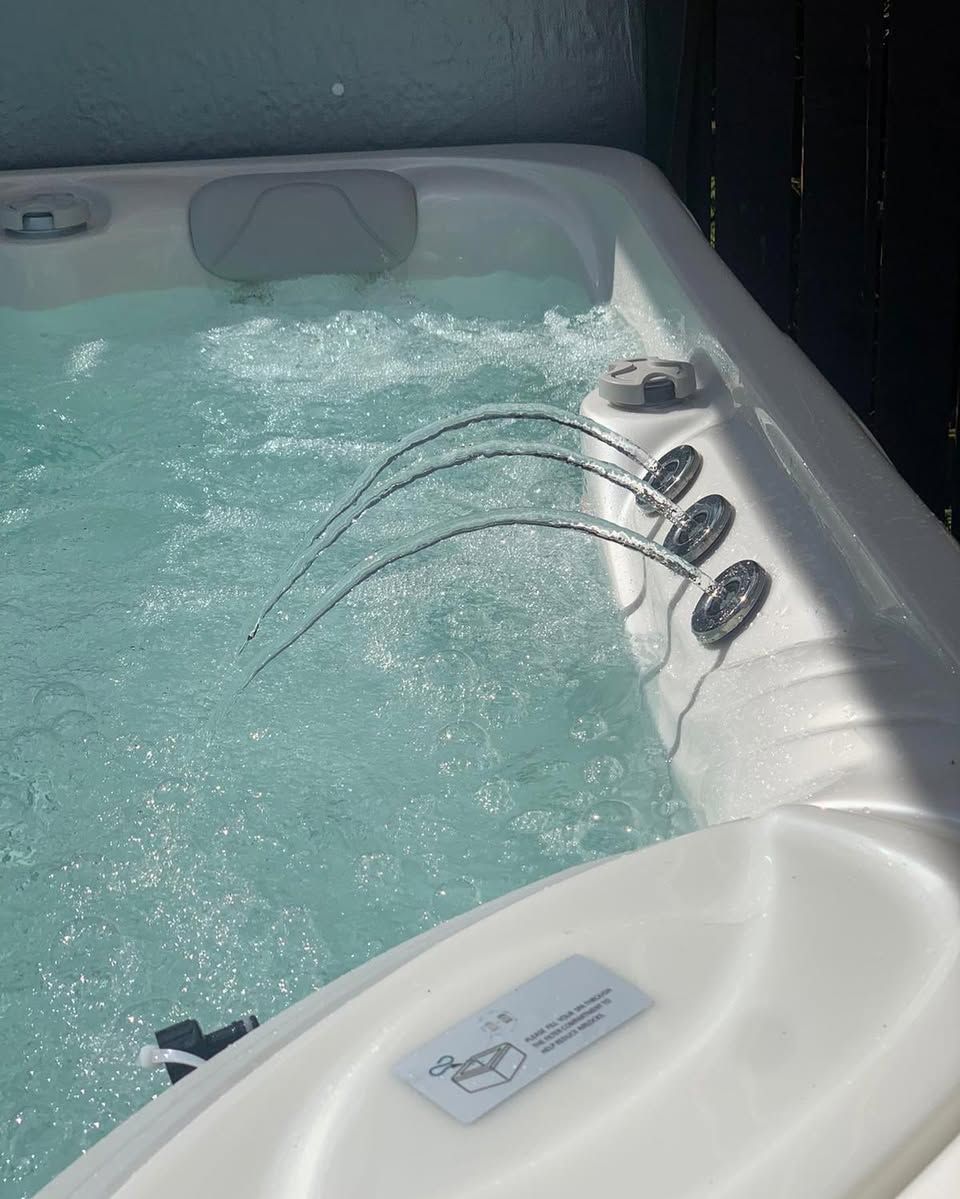 Hot tub with water jets spraying into bubbling water. White interior, outdoors.