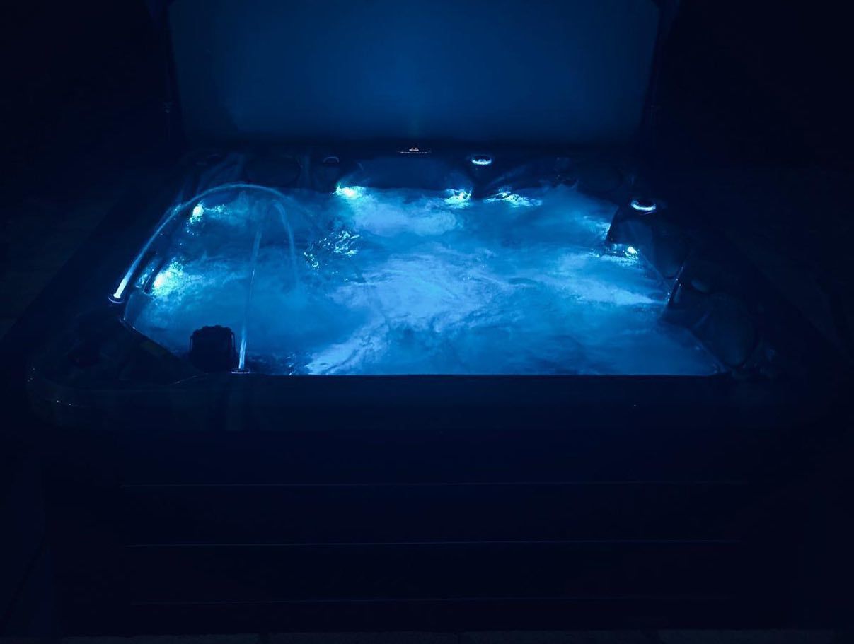 A lit-up hot tub with blue water in a dark setting.