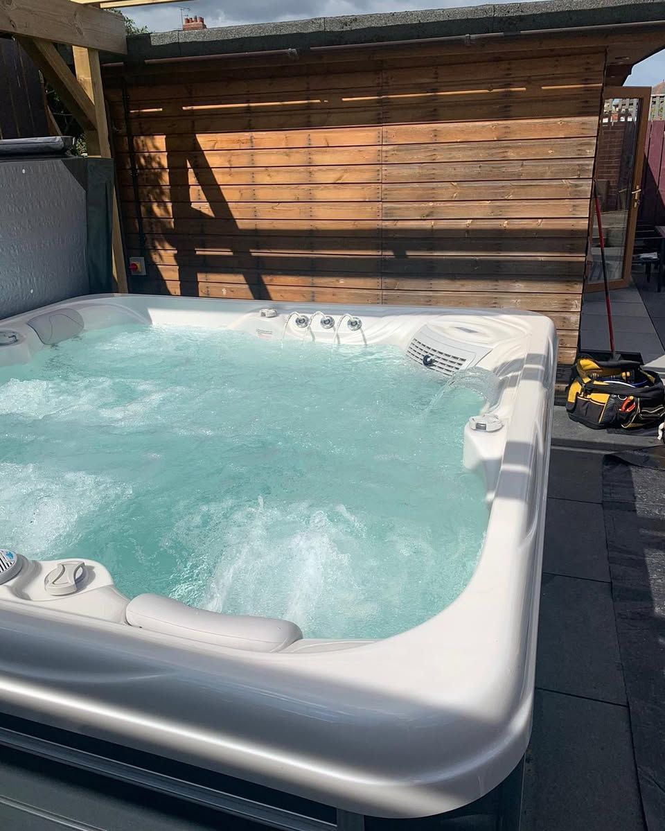A bubbling white hot tub with clear water, outdoors near a wooden fence.