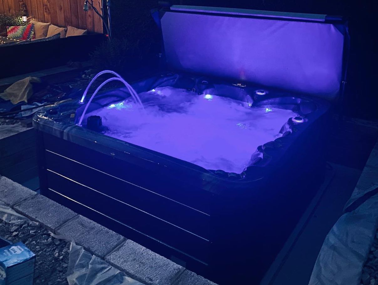 Lit-up hot tub with blue lights at night. Water is bubbling. Cover is open.