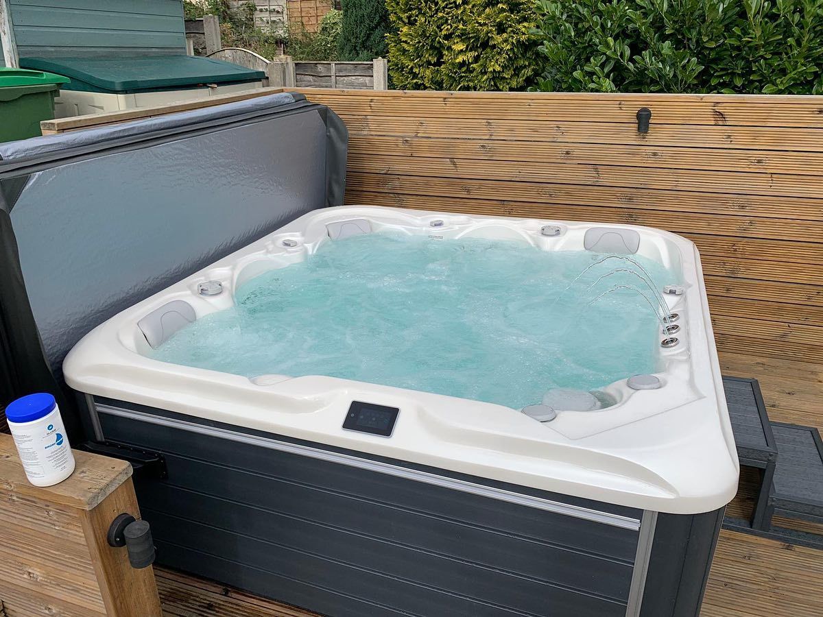Hot tub with bubbly water on a wooden deck, covered lid to the left, blue bottle next to it.