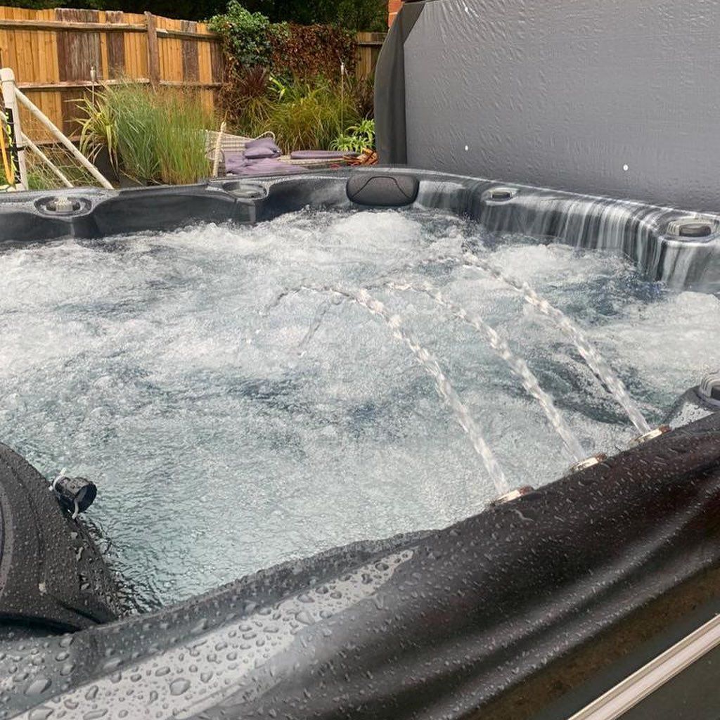 A hot tub with water jets, bubbling water, and a partially open cover, outdoors near a wooden fence.