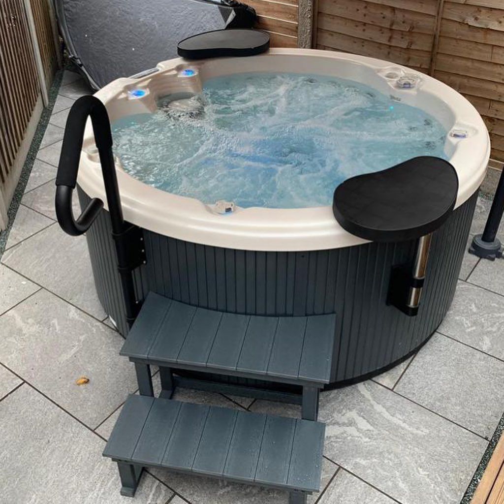 Round hot tub with gray steps and seating, bubbling water. Outdoor setting.