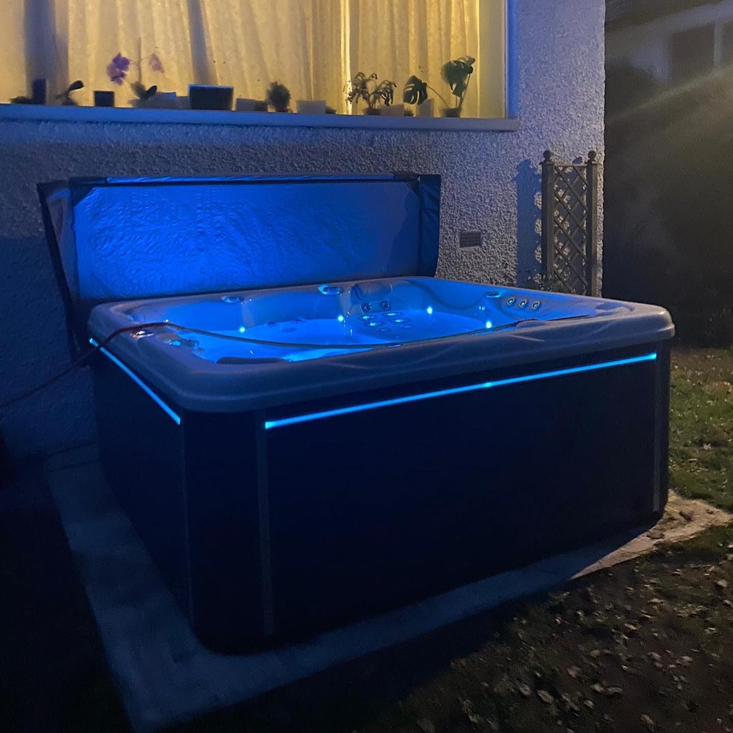Lit-up hot tub with blue lights outdoors at night. Cover open, water visible.