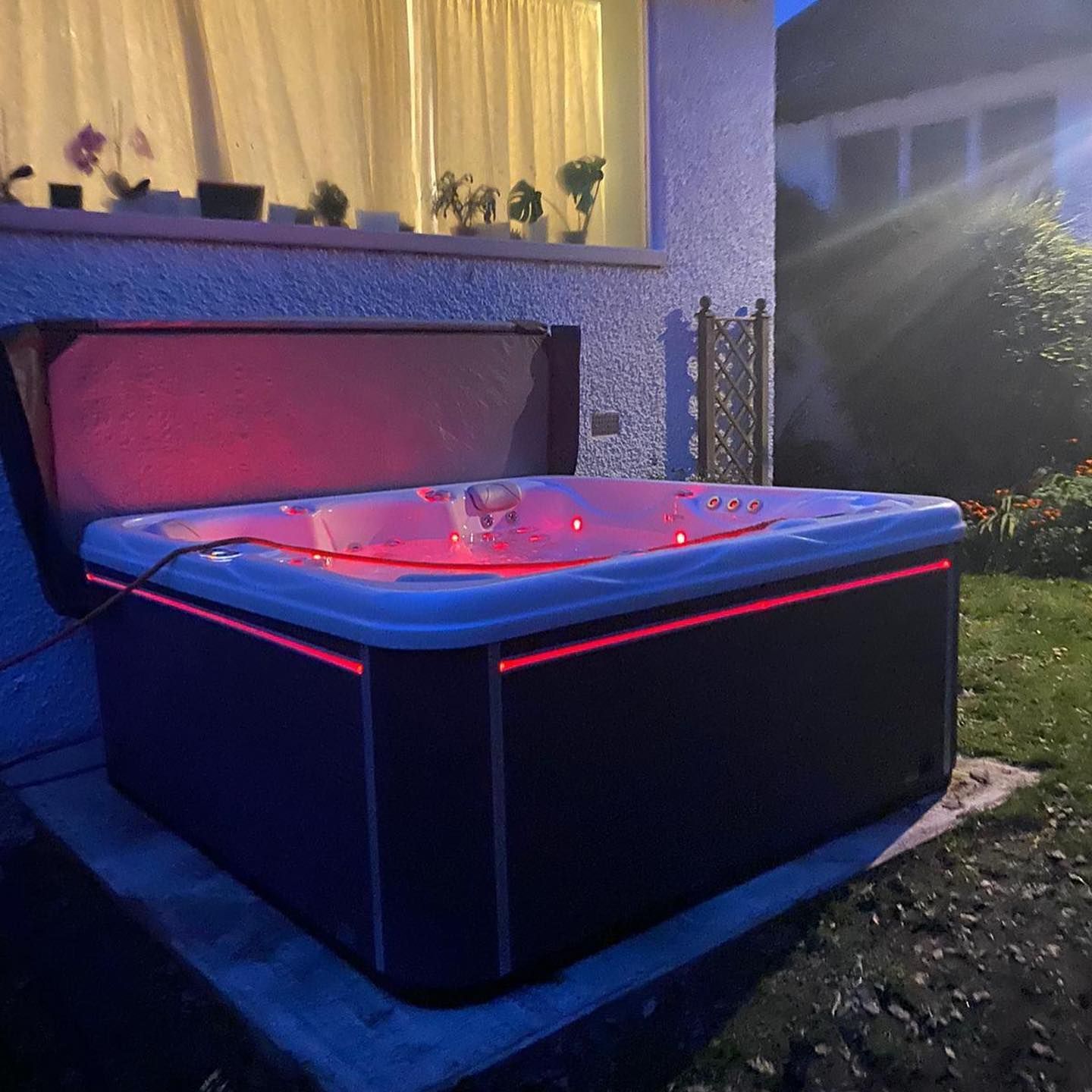 Hot tub lit with red lights, set against a house at dusk.