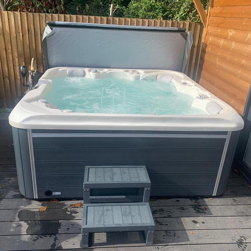 Hot tub with cover open, set on a wooden deck with steps leading up to it.