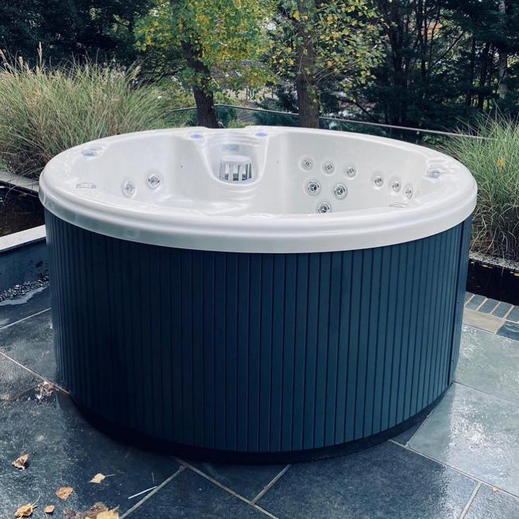 Round, blue-sided hot tub with a white interior, on a patio surrounded by plants.