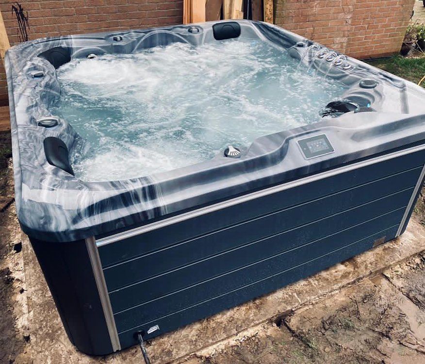A rectangular hot tub with dark blue siding and a gray marbled top, filled with bubbling water, outdoors.
