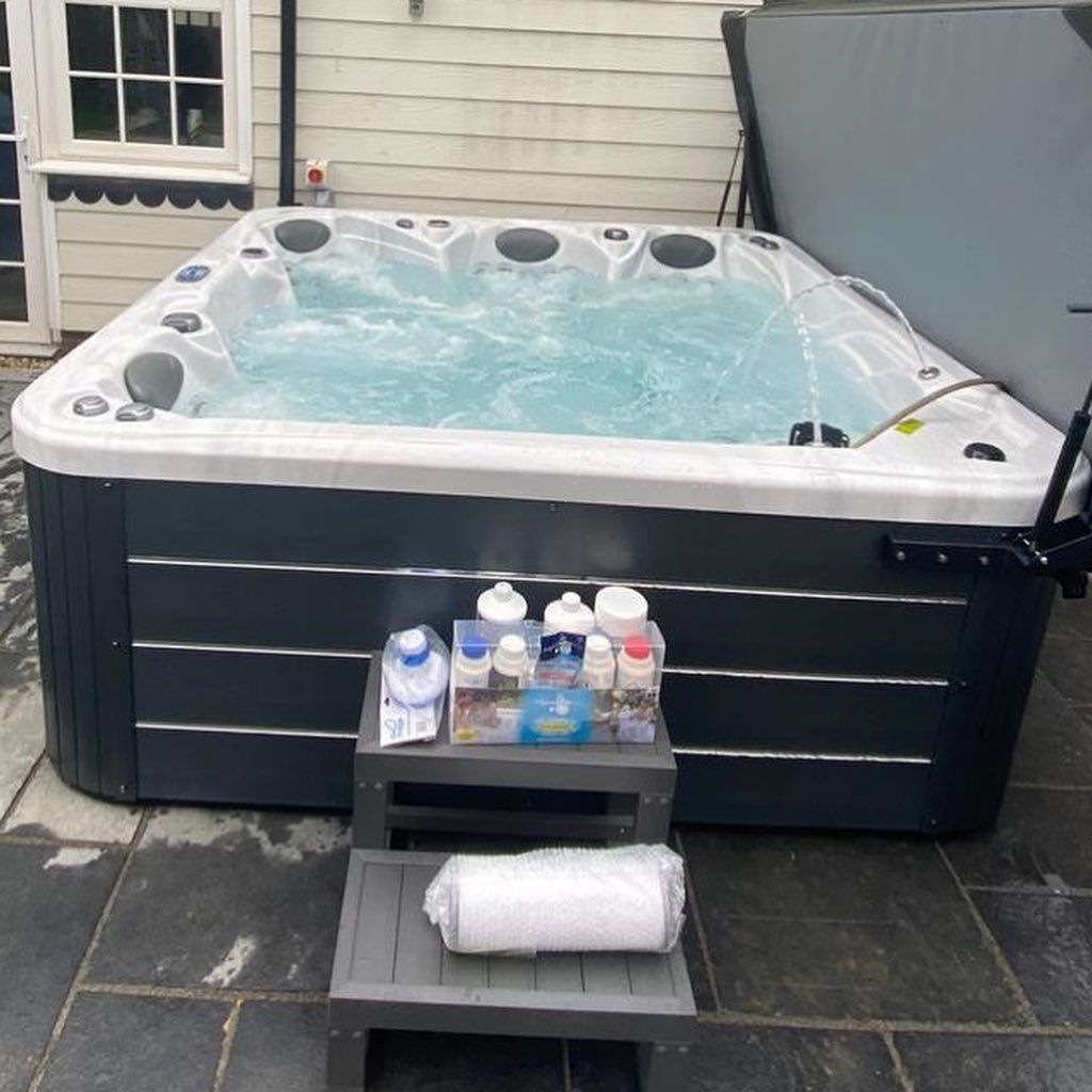 Hot tub filled with water, surrounded by chemicals and a rolled towel on a small step. Outdoors.
