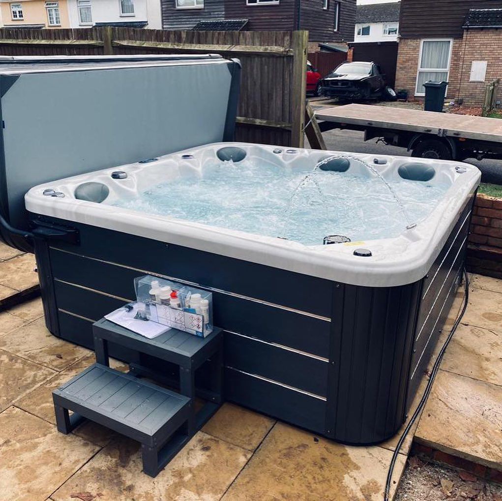 A gray hot tub in a backyard, with water bubbling and a step stool in front.