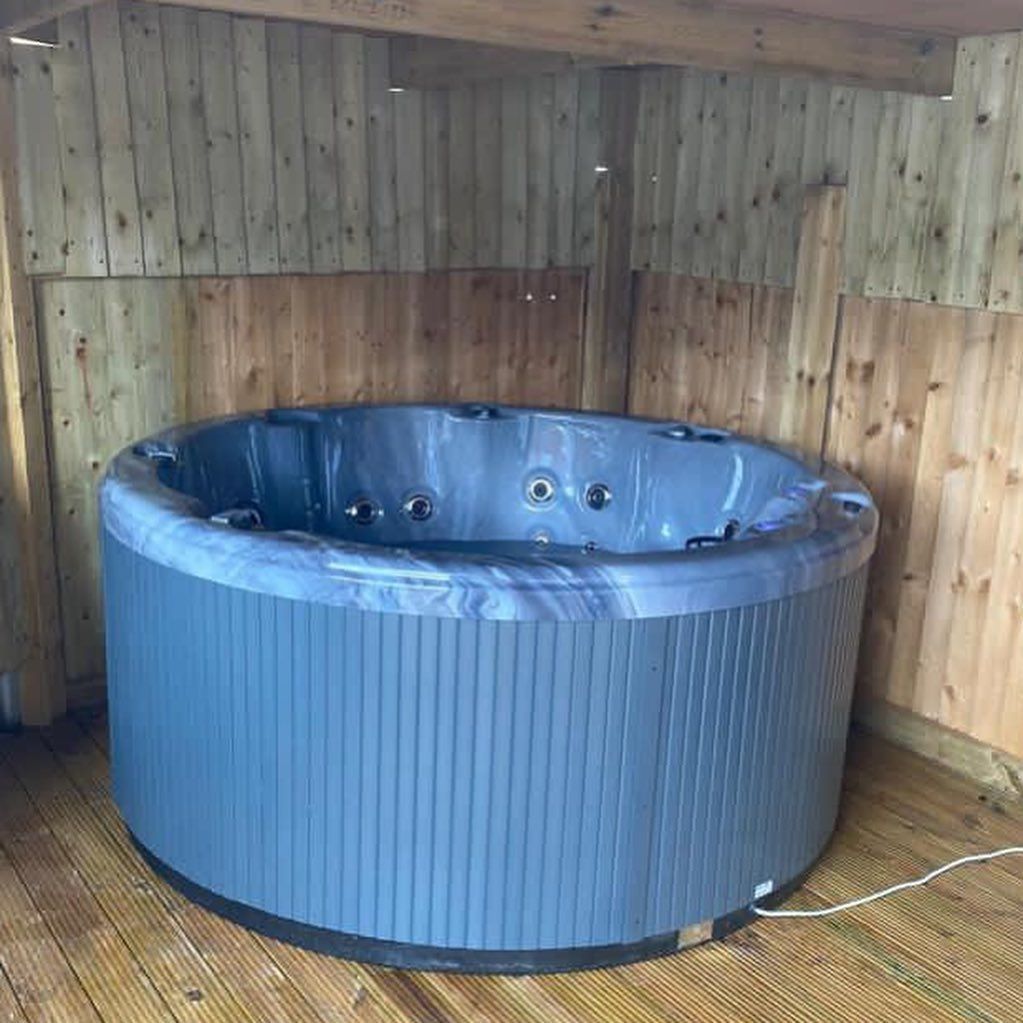 Round, gray hot tub inside a wooden structure with a wooden floor.