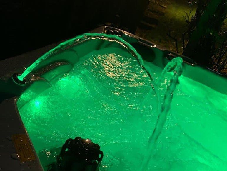 Green lit hot tub with water cascading from jets.