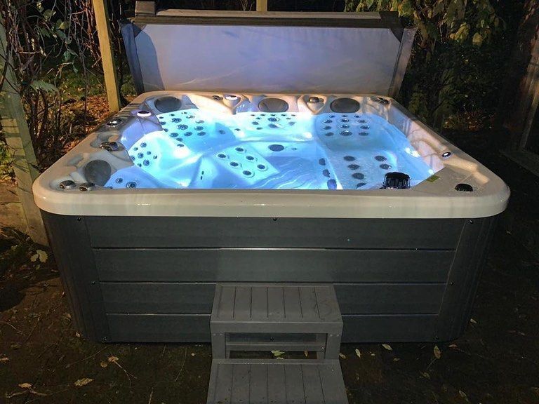 Lit hot tub at night with the cover open. A gray step stool is in front.