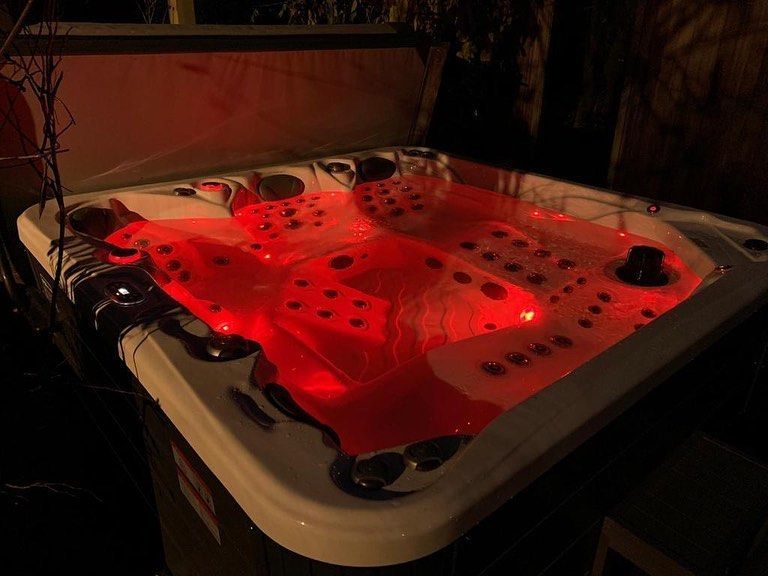 Lit-up red hot tub at night. White trim, black jets.