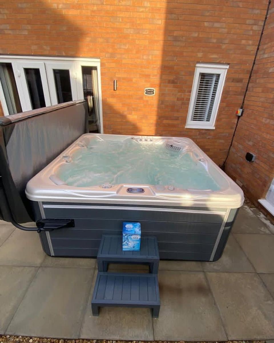 Hot tub on a patio with a step stool and brick wall background.