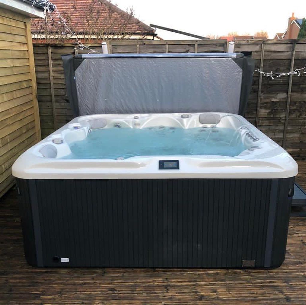 Hot tub filled with water, cover partially open, situated on a wooden deck in a backyard setting.