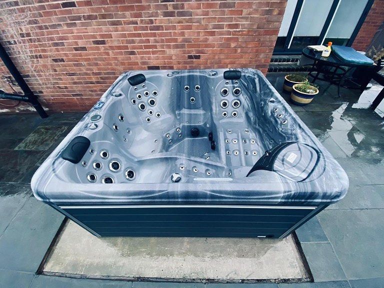 Hot tub with gray interior and dark blue exterior on a stone patio, brick wall in background.