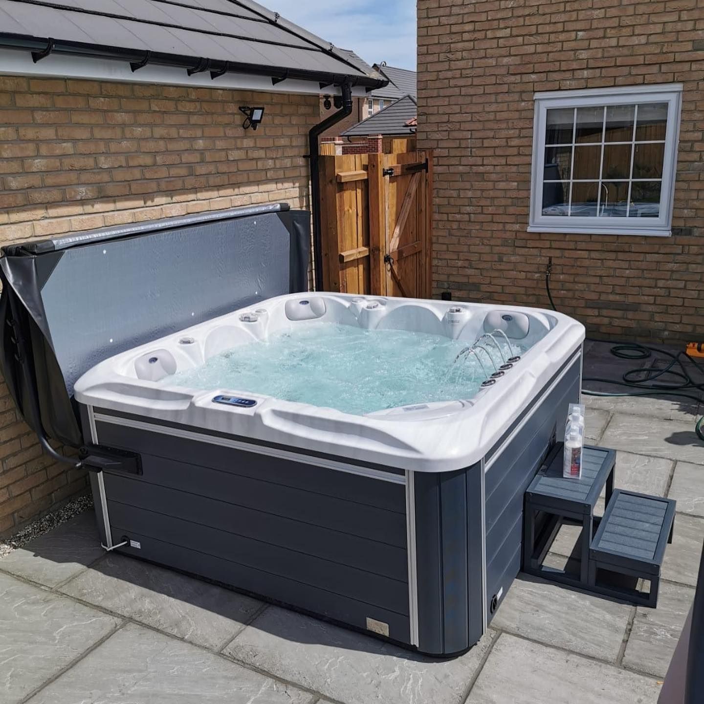 Hot tub on a stone patio next to a house. The cover is open, and water is bubbling.