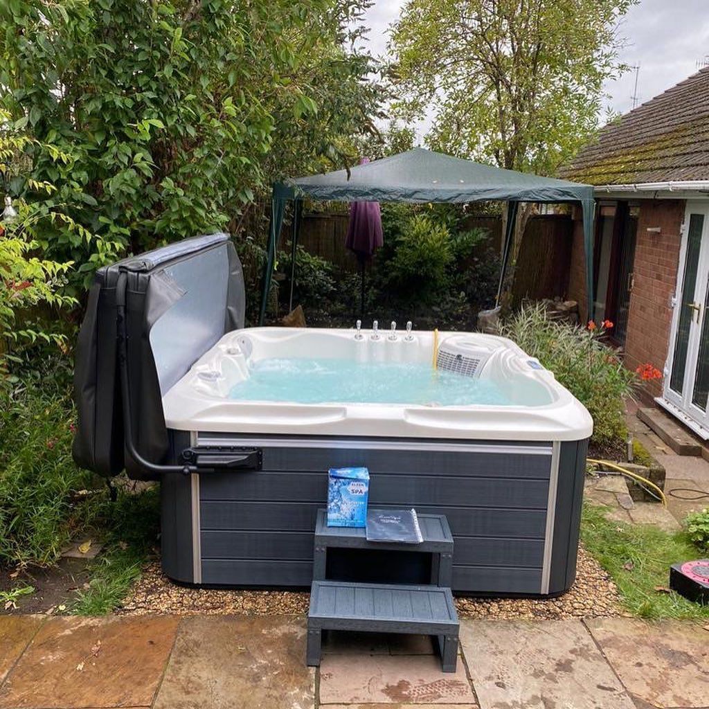 Hot tub in a backyard with cover open, steps, and gazebo in background.