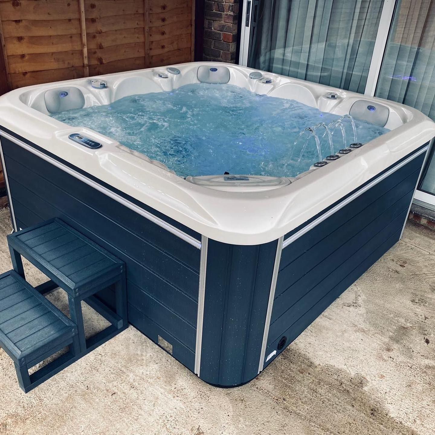 Hot tub with bubbling water, blue exterior, white trim, and step stool on a patio.
