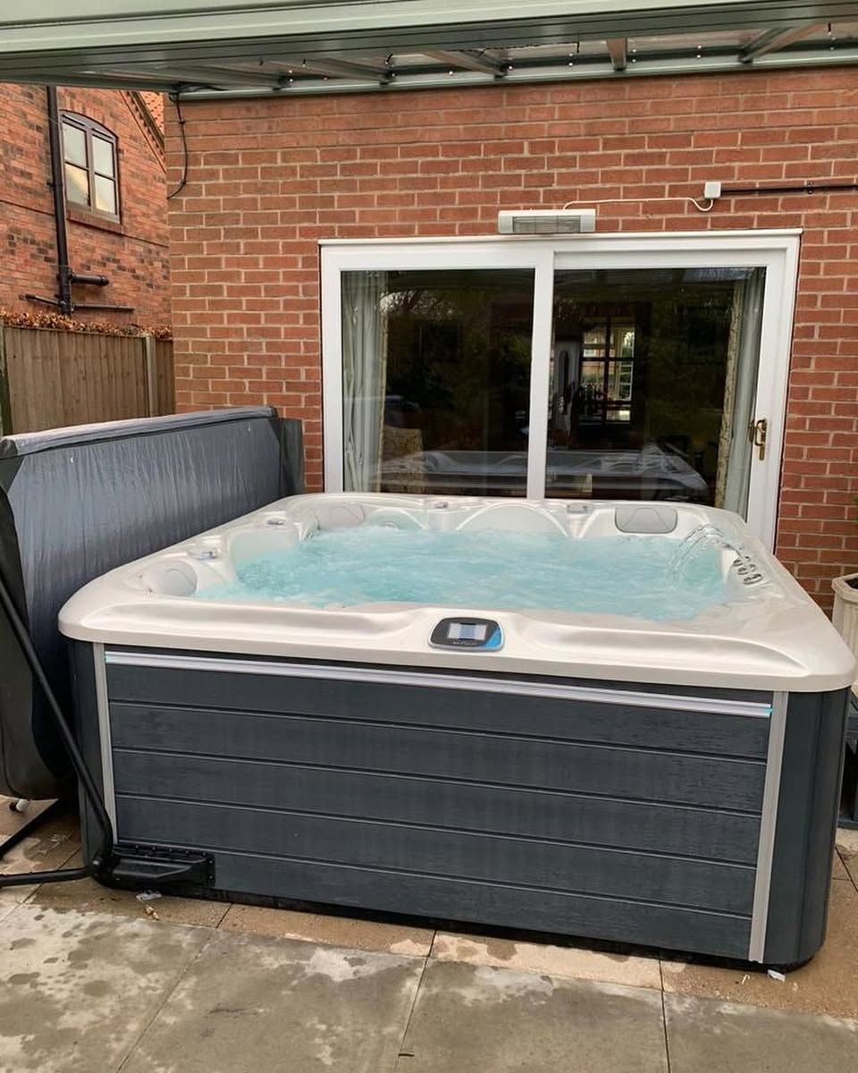 Hot tub filled with water on a patio next to a brick wall and sliding glass door.