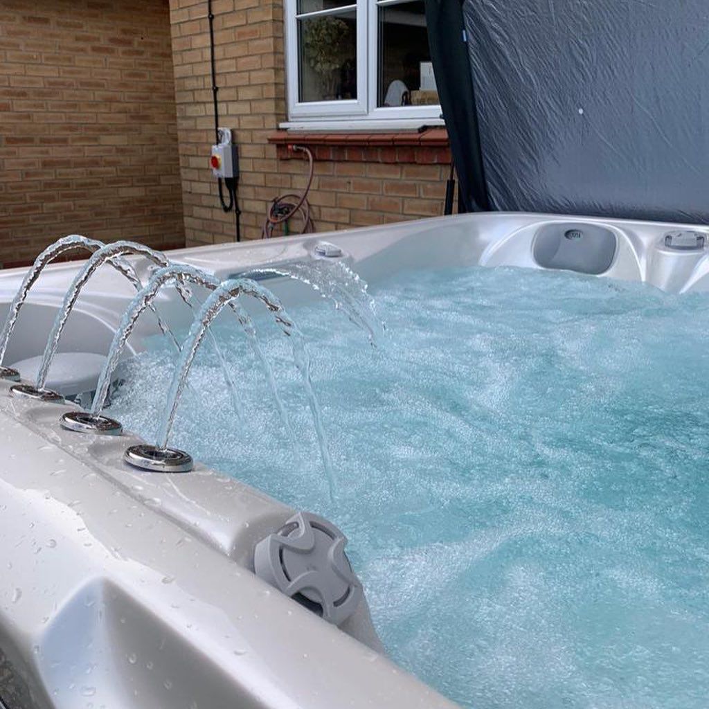 A white hot tub with water jets is outdoors, next to a brick building.