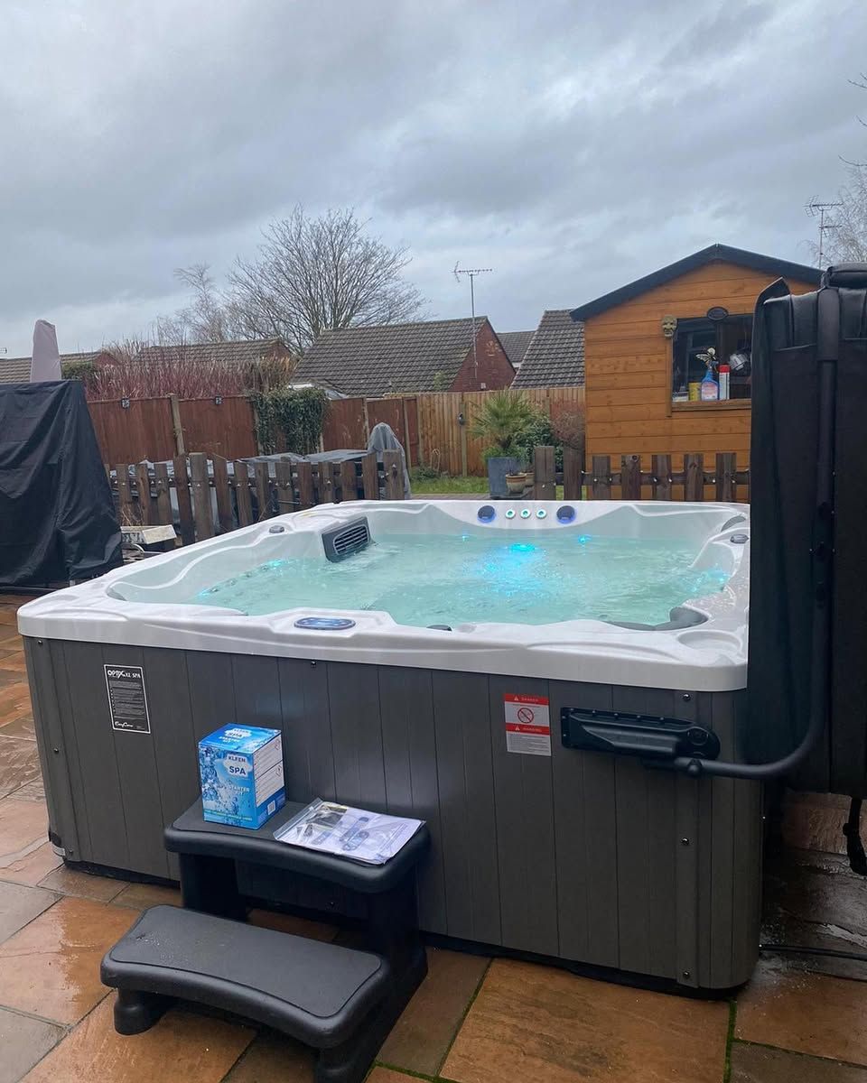Hot tub on a patio with steps, cloudy sky, and a small shed in the background.
