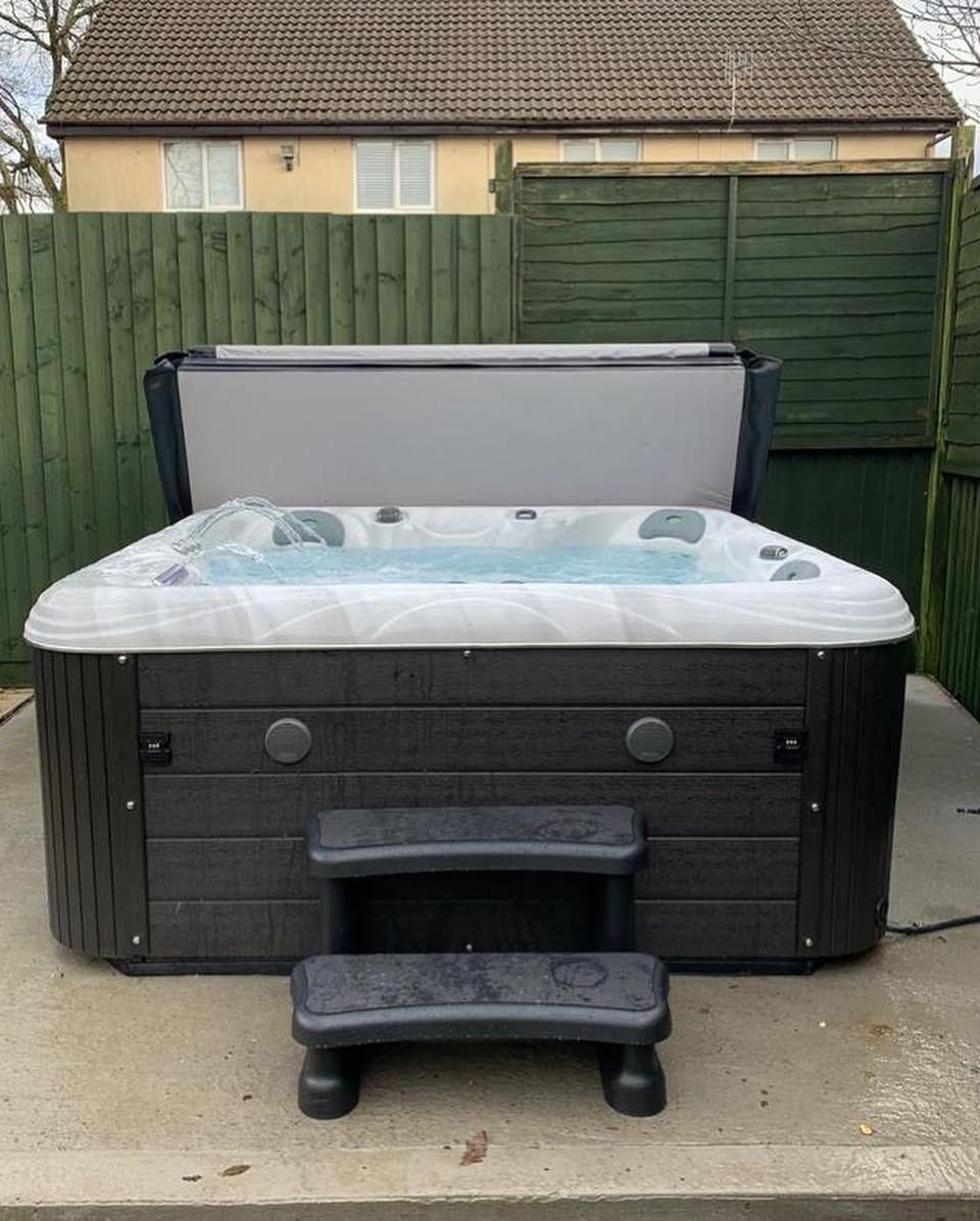 Black hot tub with steps in a backyard setting.