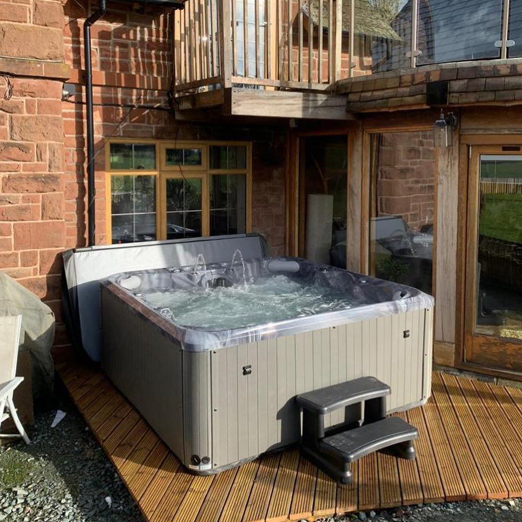 Hot tub on wooden deck outside brick building; water bubbling.