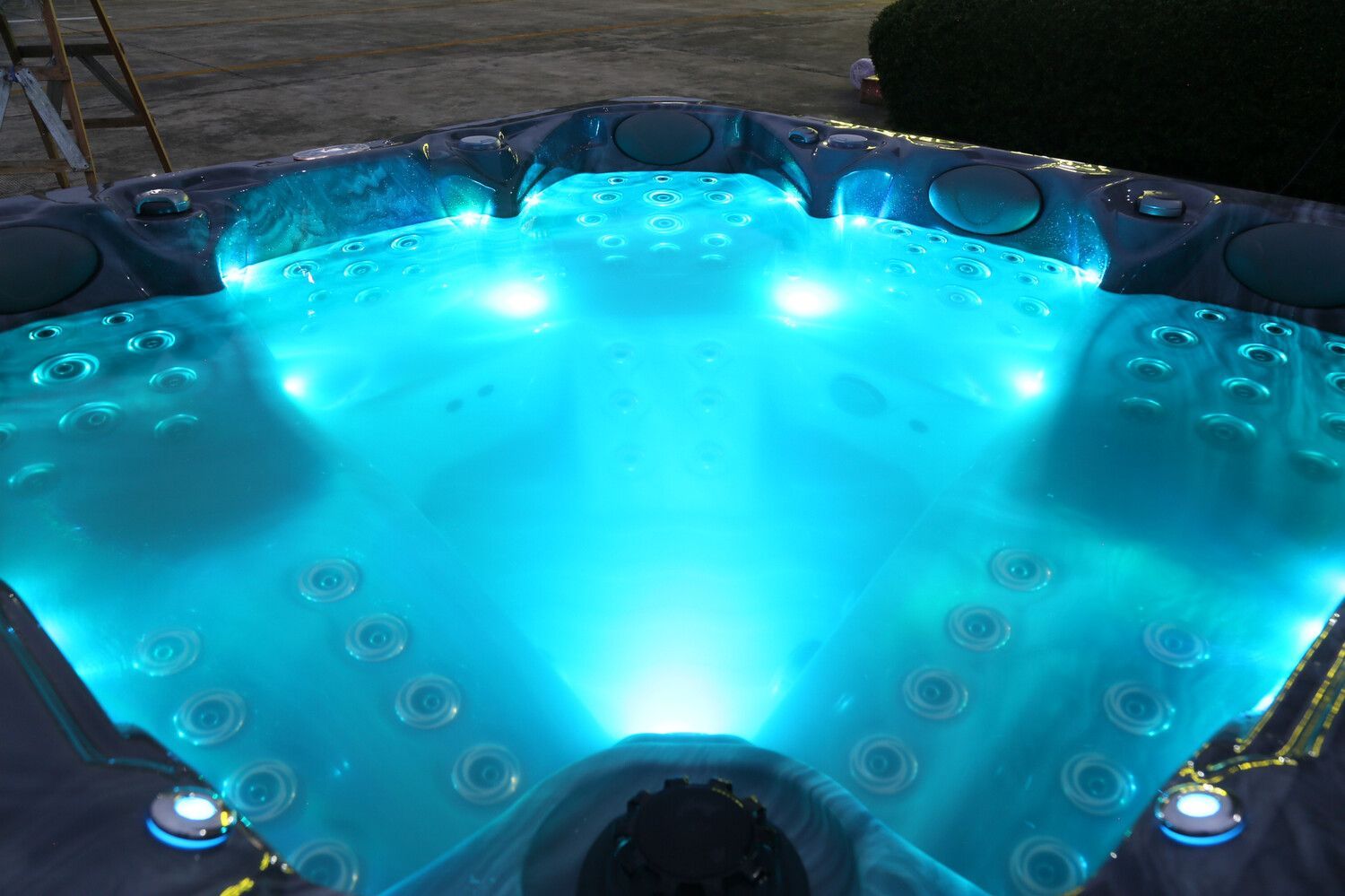 Lit up blue hot tub with jets, nighttime setting.