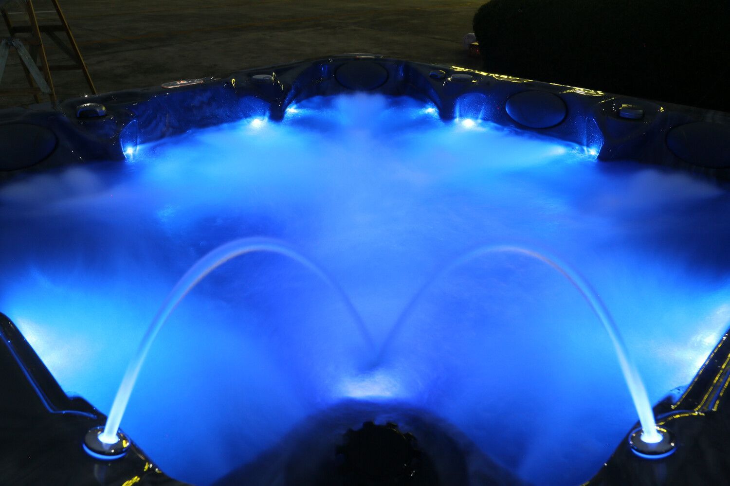 Blue-lit hot tub with water jets spraying upwards, surrounded by ambient blue lights.