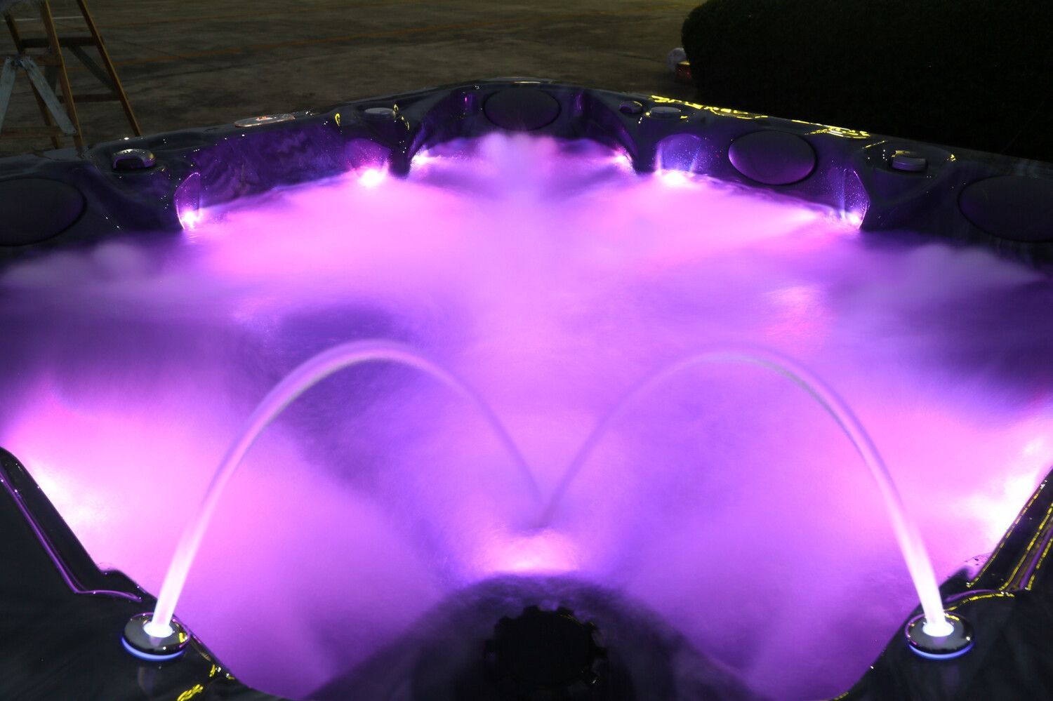 Lit up hot tub with purple lights and water fountains.