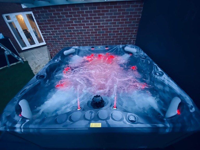 Lit hot tub with red and white jets against a dark backdrop.