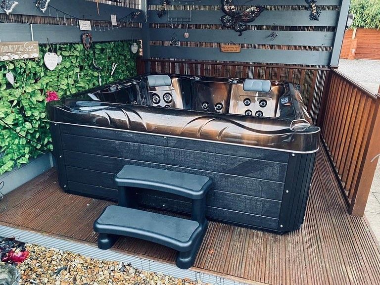 Black hot tub with steps, set on a wooden deck in a backyard.