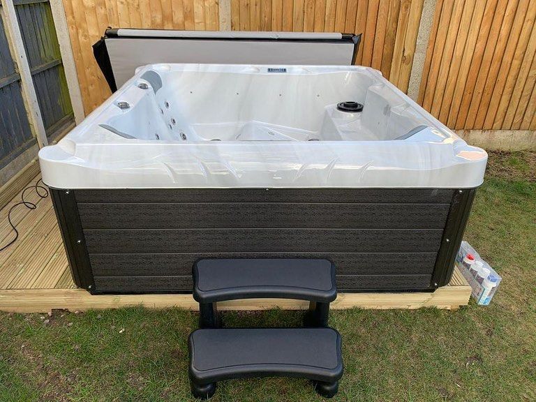 Hot tub with dark gray exterior, steps, and a partially open cover, in a backyard setting.