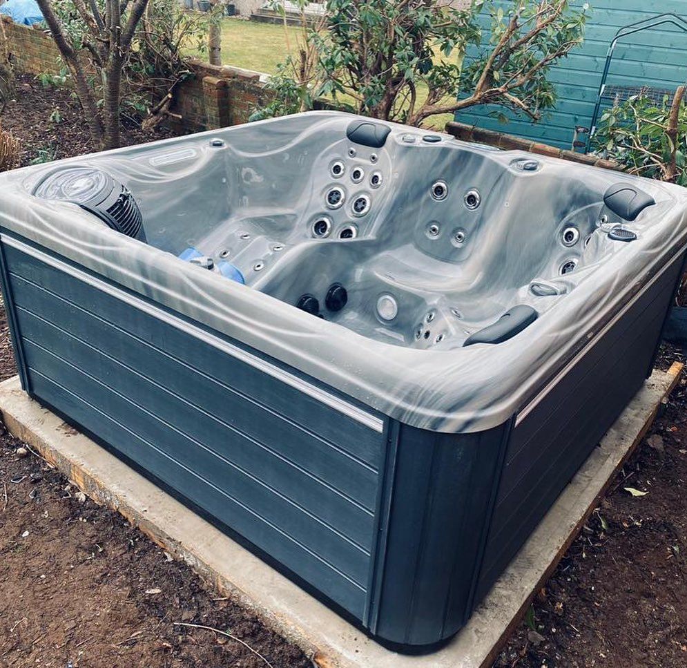 A gray and blue hot tub on a concrete base, outdoors in a yard.