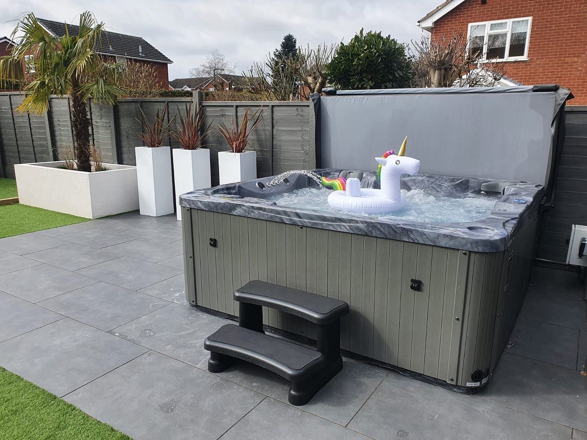 Hot tub with a unicorn float on a patio with artificial grass and potted plants.