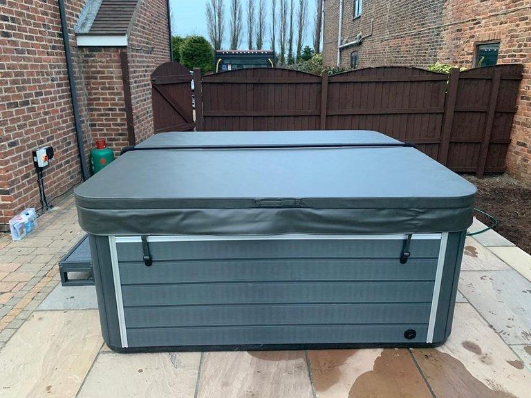 Hot tub with gray cover on patio with brick and wood fencing.