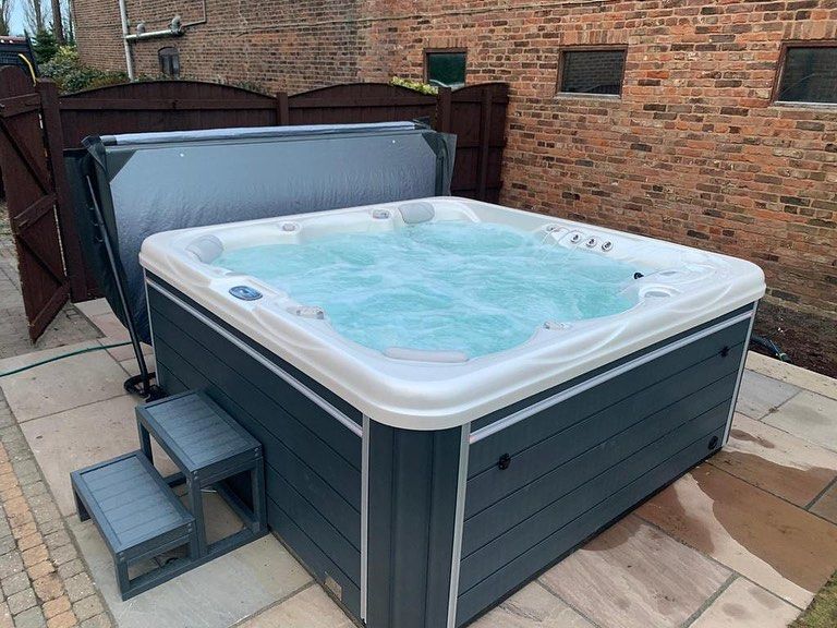Hot tub with bubbling water, gray siding, white trim, steps, and open cover; set on a patio.