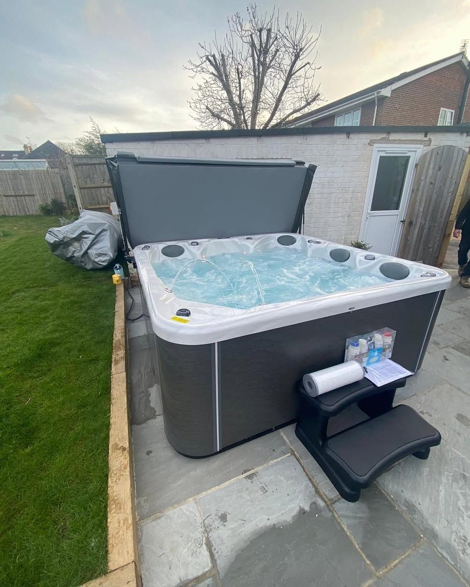 Hot tub with the cover open in a backyard. A gray hot tub with water and a step stool.