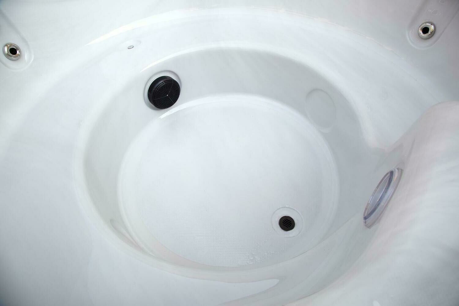 Close-up of a white hot tub interior with a central well containing a drain and jets.