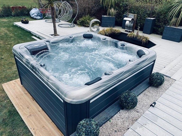 A hot tub with bubbling water on a wooden deck in a yard with landscaping.