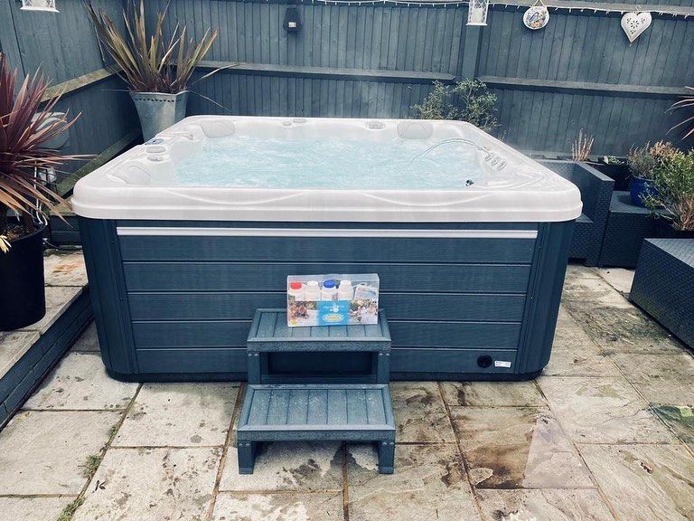 Hot tub on a patio; dark gray exterior, white trim, steps in front.