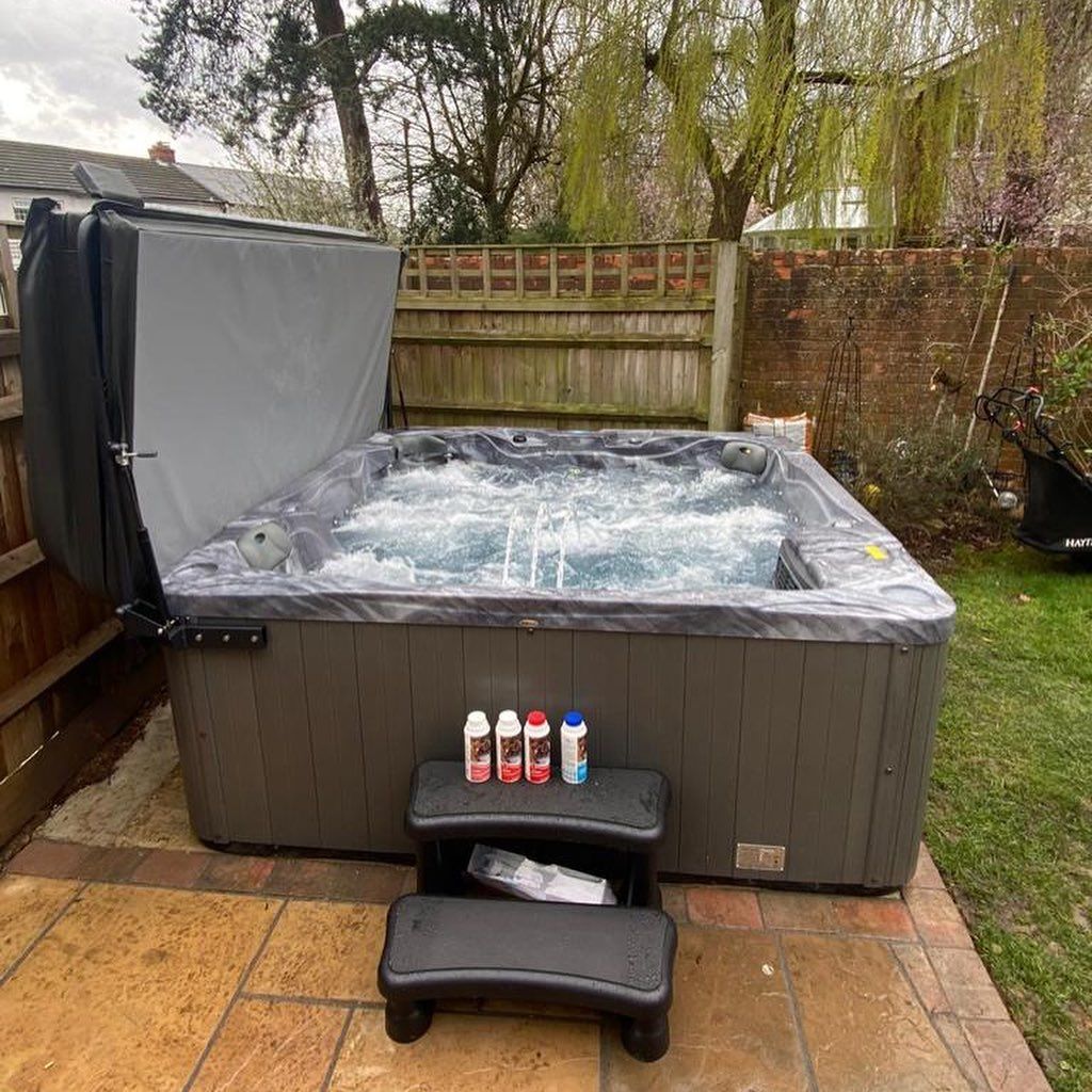 Hot tub with cover open, on a patio. Chemicals on steps in front. Bubbling water.