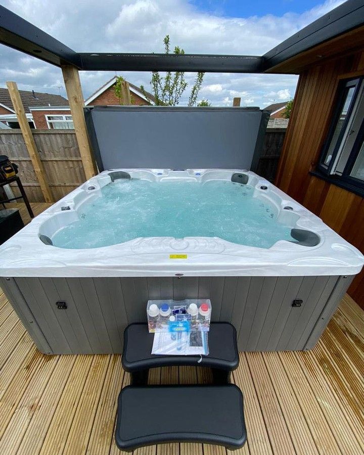 Hot tub filled with water on a wooden deck, covered by a partial roof. Chemicals and steps are in front.