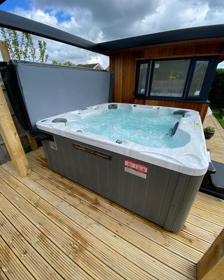 Hot tub on wooden deck, under wooden structure. Water bubbling, cover partially open.