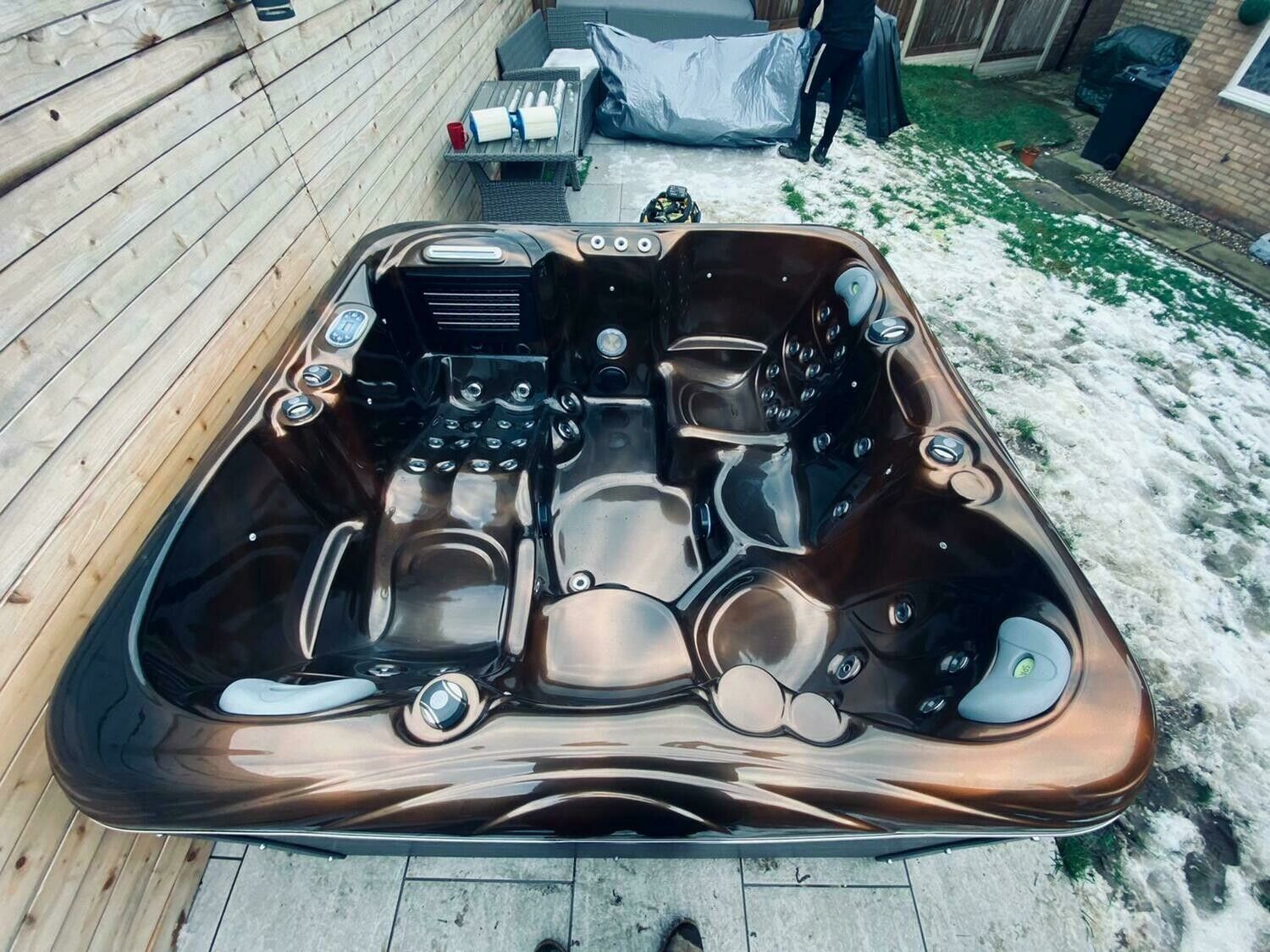 Dark brown hot tub, partially covered by snow, set on wooden decking.