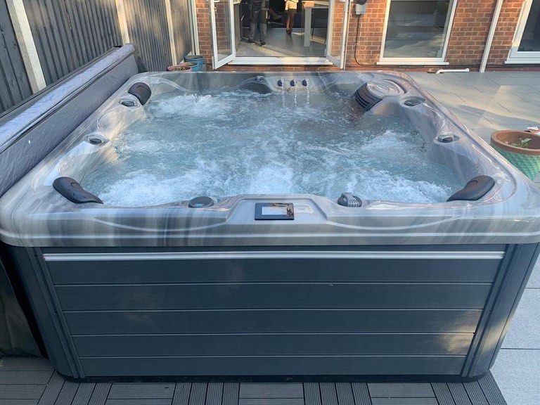 Square hot tub filled with bubbling water on a wooden deck. Gray and black tones.
